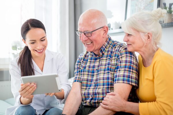 Nurse showing medical raport using tablet to senior couple at home