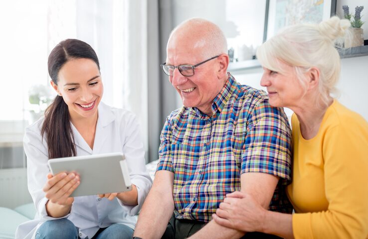 Nurse showing medical raport using tablet to senior couple at home