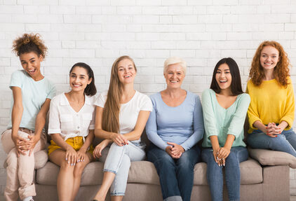 Lächelnde Frauen sitzen auf einem Sofo vor einer weißen Wand