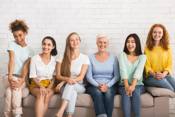 Lächelnde Frauen sitzen auf einem Sofo vor einer weißen Wand