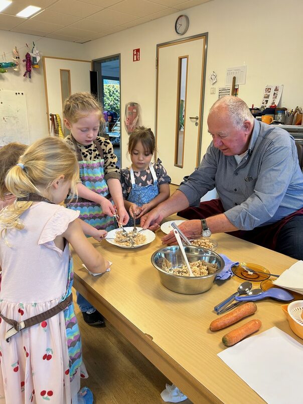 Ein älterer Herr und einige Kinder sitzen bzw. stehen an einem Tisch und bereiten einen Dip vor