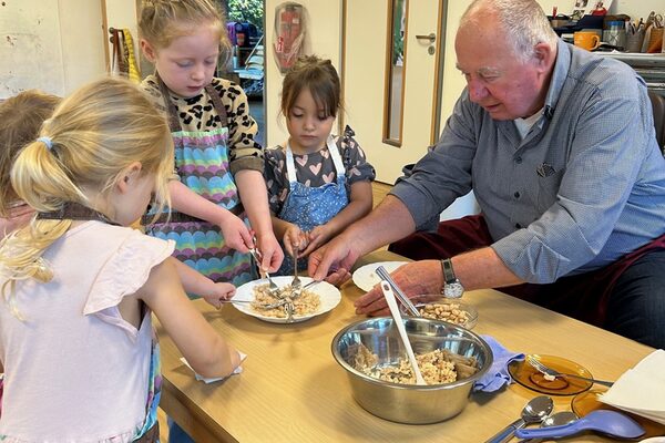 Ein älterer Herr und einige Kinder sitzen bzw. stehen an einem Tisch und bereiten einen Dip vor