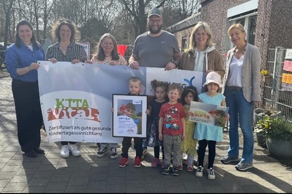 Erwachsene halten ein Banner mit der Aufschrift KITA Vital in die Höhe und einige Kinder stehen davor