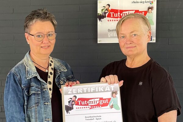 Zwei Frauen halten gemeinsam einen Bilderrahmen mit einem Zertifikat in den Händen