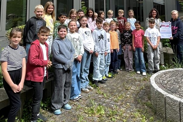 Eine Gruppe von Kindern steht im Bogen vor einer fensterfront. Hinten rechts stehen zwei Erwachsene mit einem Zertifikat in der Hand