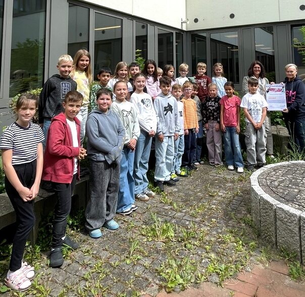 Eine Gruppe von Kindern steht im Bogen vor einer fensterfront. Hinten rechts stehen zwei Erwachsene mit einem Zertifikat in der Hand