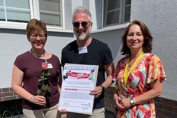 Zwei Frauen und ein Mann in der Mitte des Bildes halten einen Bilderrahmen mit einem Zertifikat in den Händen