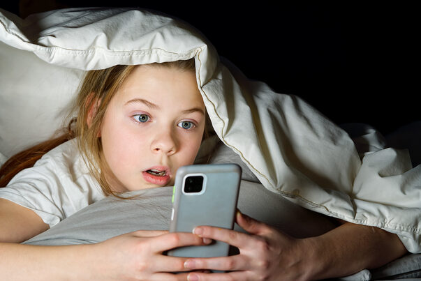 Portrait of girl with mobile phone under blanket at night. Gadget night. Social media addiction. Online communication.