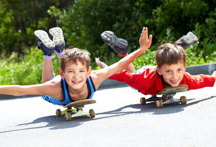 Zwei Kinder liegen auf einem Skateboard