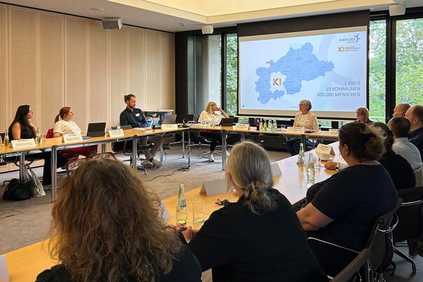 Blick in den Sitzungstraum. Zu sehen sind die Teilnehmenden und eine Präsentation im Hintergrund.