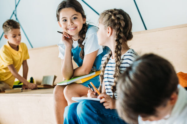 group of schoolchildren with notebooks studying on tribune at school corridor